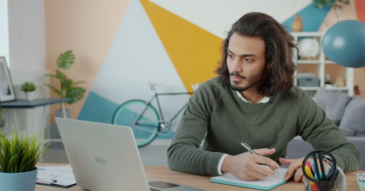 Business owner working at a desk with a laptop and notebook while reviewing notes and planning next steps.